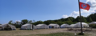 Eine Reihe Zelte auf grüner Wiese mit einer roten Fahne auf dem Dorfplatz